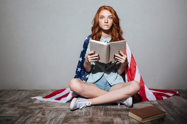 Choqué jeune femme rousse lecture livre portant le drapeau américain