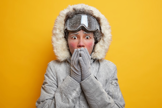 Choqué, une jeune femme stressée couvre la bouche avec les mains porte une veste à capuche et des gants recouverts de givre se sent froid pendant les activités de plein air saisonnières en Scandinavie.