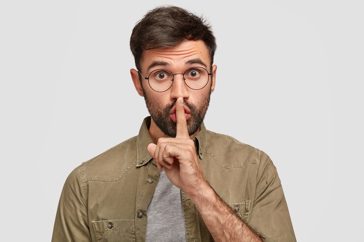 Photo gratuit choqué, jeune homme barbu fait signe de silence, regarde secrètement, effrayé par des rumeurs inattendues, isolé sur un mur blanc. chut, tais-toi! concept de secret et langage corporel