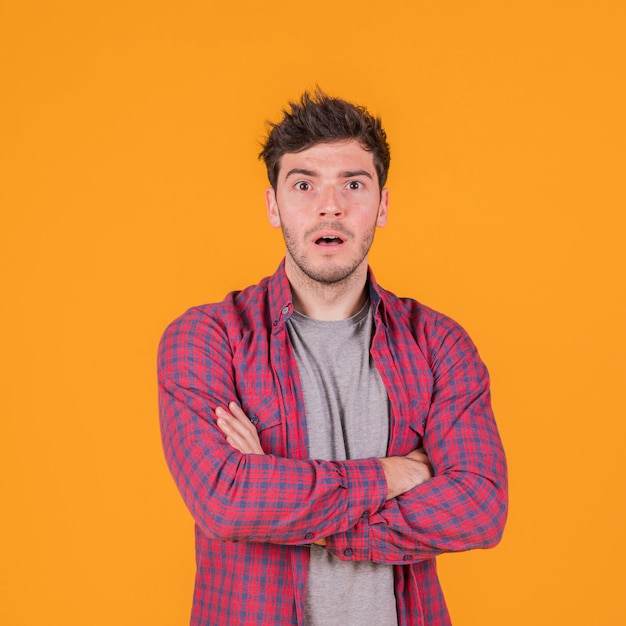 Choqué jeune homme avec son bras croisé contre un fond orange