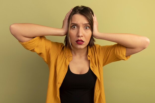 Choqué jolie femme caucasienne tient la tête sur vert olive