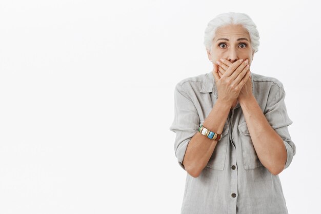 Choqué mamie sans voix ferme la bouche avec les mains et le regard