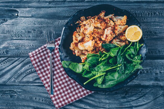 Chou-fleur frit dans une assiette avec des verts vue de dessus sur un tissu de pique-nique et fond en bois foncé