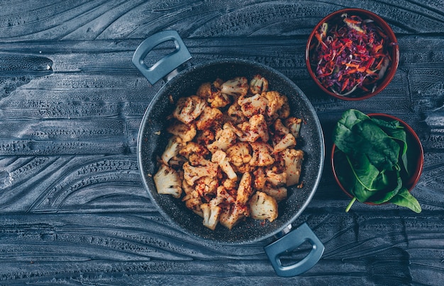 Chou-fleur frit dans une casserole avec salade de légumes, vue de dessus vert sur un fond en bois foncé. espace pour le texte