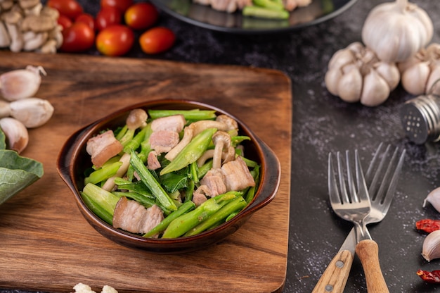 Chou frit et poitrine de porc sautés dans une assiette posée sur une assiette en bois.