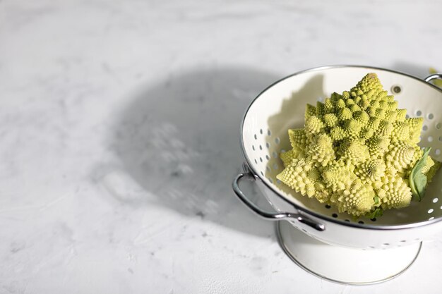 Chou romanesco dans une passoire blanche sur fond gris BIOVegetables Copy Space