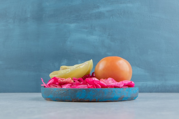 Photo gratuite chou rouge fermenté, tomates entières et tranchées dans une assiette en bois