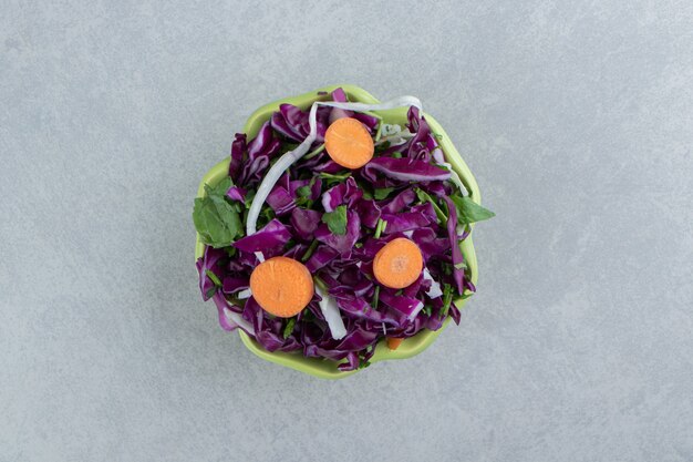 Chou rouge râpé, légumes verts et carottes dans un bol, sur le marbre.