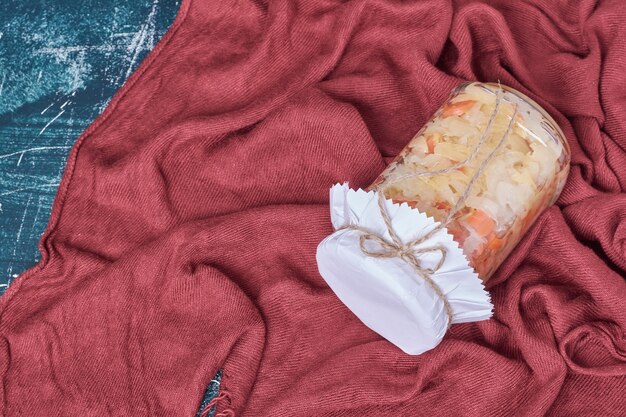 Choucroute en bocal en verre sur bleu avec nappe rouge.