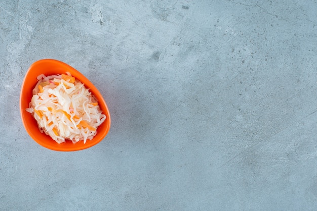 Choucroute fermentée aux carottes dans un bol en plastique , sur la table bleue.