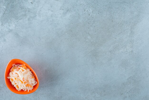 Choucroute fermentée aux carottes dans un bol en plastique , sur la table bleue.