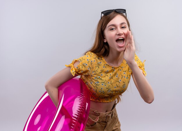 Chuchotant jeune fille portant des lunettes de soleil sur la tête tenant l'anneau de bain mettant la main près de la bouche sur un mur blanc isolé