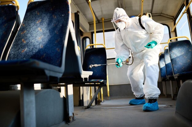 Ci-dessous, vue d'un homme en tenue de protection faisant la désinfection du bus public pendant la pandémie de coronavirus