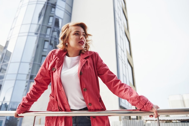 Ciel nuageux. Jolie femme adulte en manteau rouge chaud se promène dans la ville à son heure du week-end