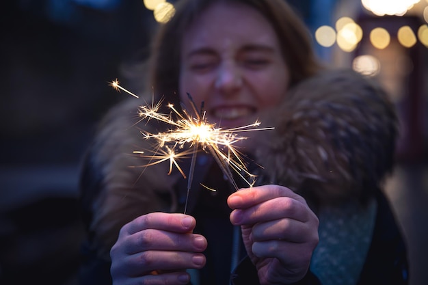 Cierges magiques brûlants dans les mains d'une jeune femme dans l'obscurité