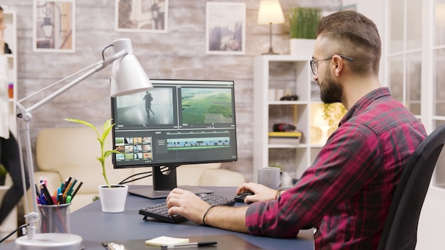 Cinéaste créatif travaillant sur la post-production d'un film tout en travaillant à domicile. La petite amie en arrière-plan marche dans la maison et parle au téléphone.