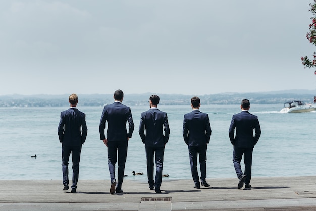 Cinq hommes en costume de classe marchent vers la mer bleue