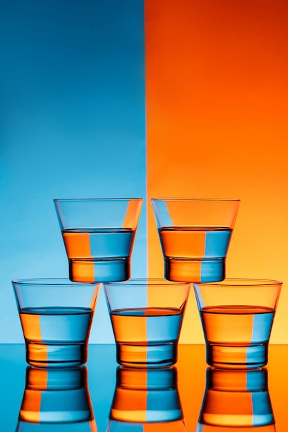 Photo gratuite cinq verres d'eau sur fond bleu et orange.