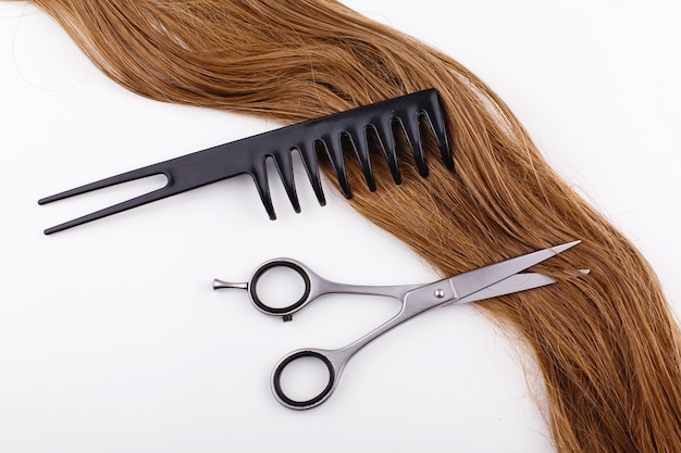 Des ciseaux en acier reposent sur la vague des cheveux bruns soyeux avec un peigne noir