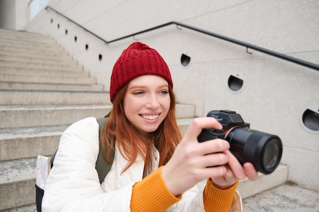 Photo gratuite les citadins et le mode de vie heureux femme rousse prend des photos tenant un appareil photo numérique professionnel phot