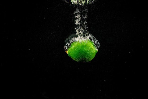 Le citron vert étincelle éclabousse l&#39;eau sur fond noir