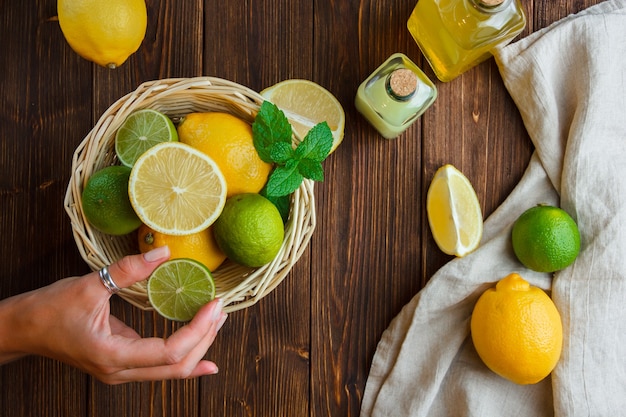 Citrons dans un panier avec un chiffon blanc main tenant la moitié du citron vue de dessus sur une surface en bois