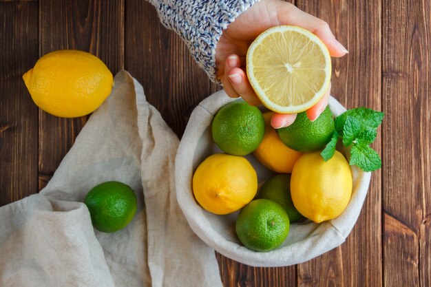 Citrons dans un panier avec un chiffon blanc, mains tenant vue de dessus de citron sur une surface en bois