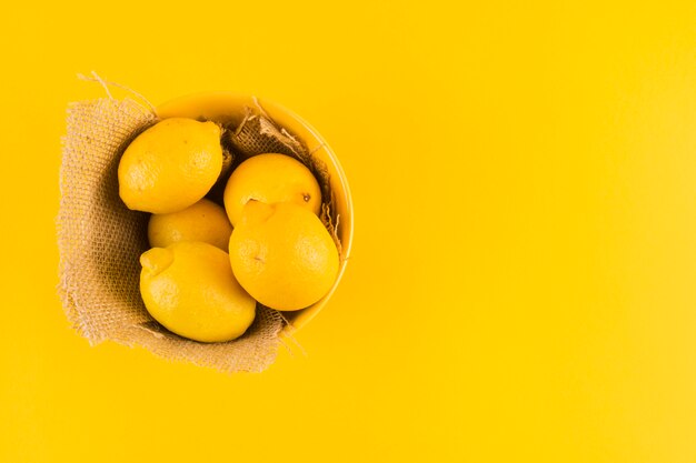 Citrons entiers dans le bol avec toile de jute sur fond jaune