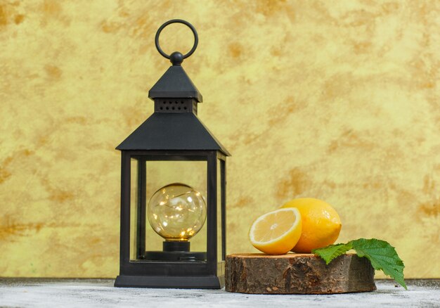 Citrons avec des feuilles et vue de côté de lampe antique sur une tranche de bois et une surface texturée