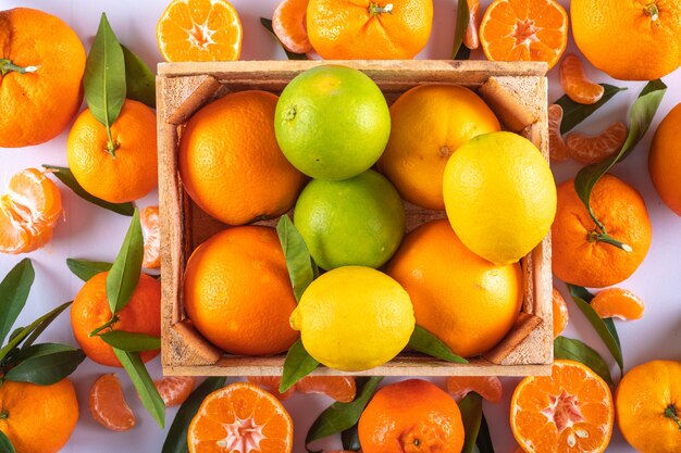 citrons mandarins et fruits orange dans une boîte en bois sur une surface blanche