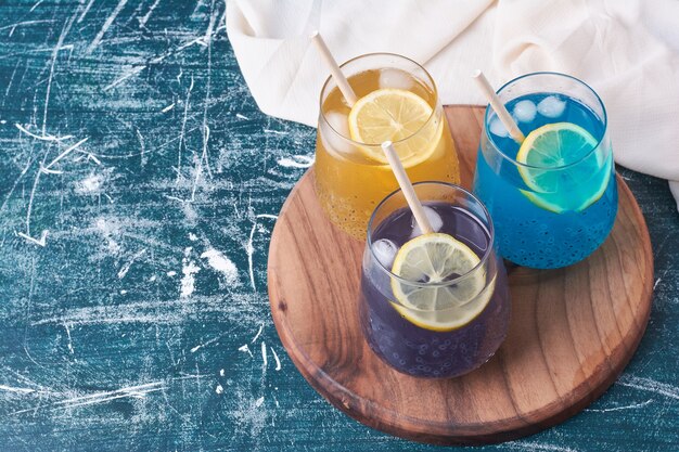 Citrons avec des tasses colorées de boisson sur bleu.