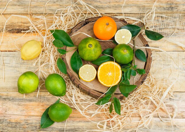 Citrons verts, oranges et mandarines dans une assiette en bois