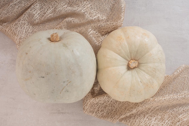 Citrouilles mûres blanches sur tableau blanc avec toile de jute.