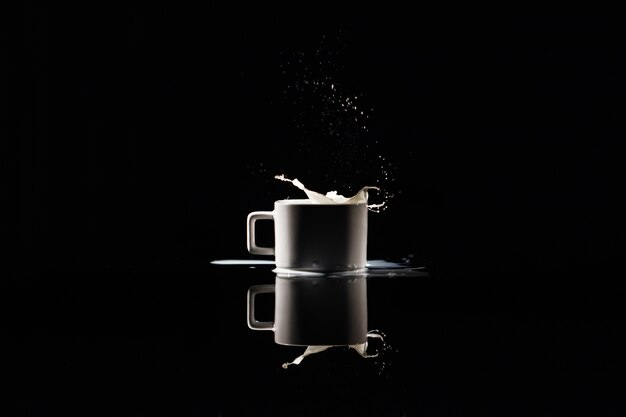 Éclaboussures de lait dans une tasse blanche sur fond noir