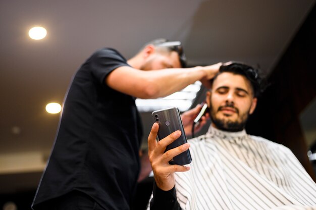 Client à angle faible chez le coiffeur vérifiant son téléphone