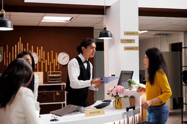 Client de l'hôtel recevant le formulaire d'inscription d'un concierge asiatique serviable. Femme asiatique d'âge moyen détendue en vacances faisant la préparation nécessaire pour l'enregistrement dans un complexe moderne