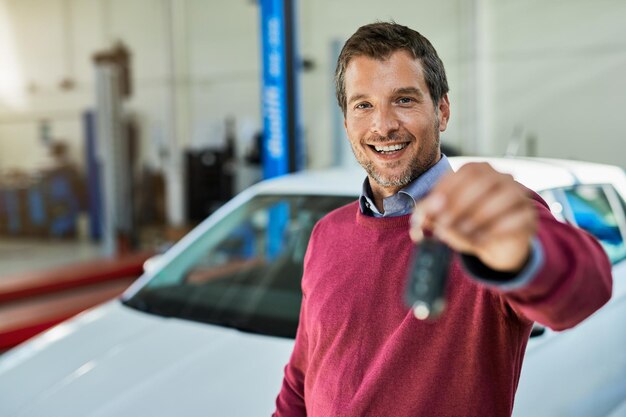 Client masculin satisfait tenant la clé de voiture dans un atelier de réparation automobile et regardant la caméra