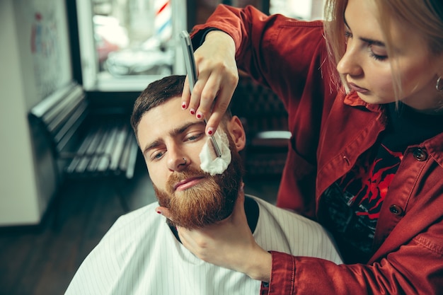 Client pendant le rasage de la barbe dans le salon de coiffure. Barbier féminin au salon. Égalité des sexes. Femme dans la profession masculine.