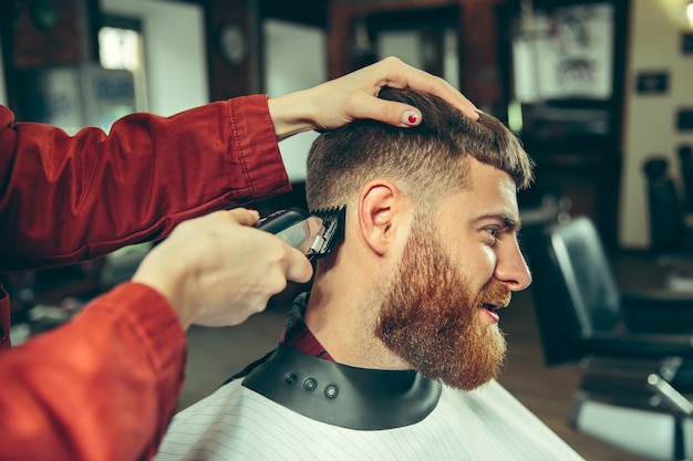 Client pendant le rasage de la barbe dans le salon de coiffure. Barbier féminin au salon. Égalité des sexes. Femme dans la profession masculine.