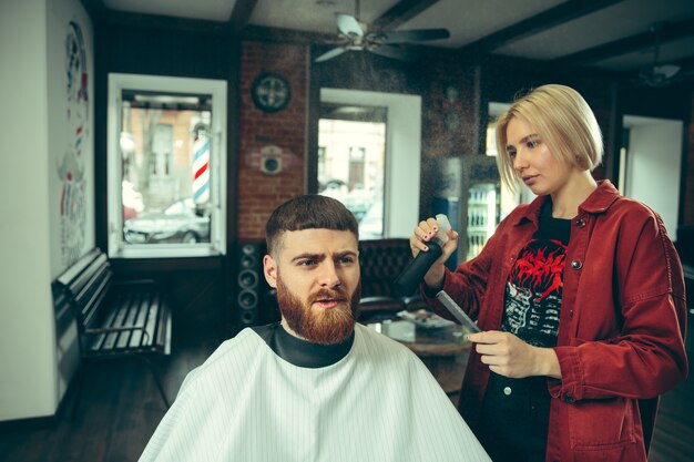 Client pendant le rasage de la barbe dans le salon de coiffure. Barbier féminin au salon. Égalité des sexes. Femme dans la profession masculine.