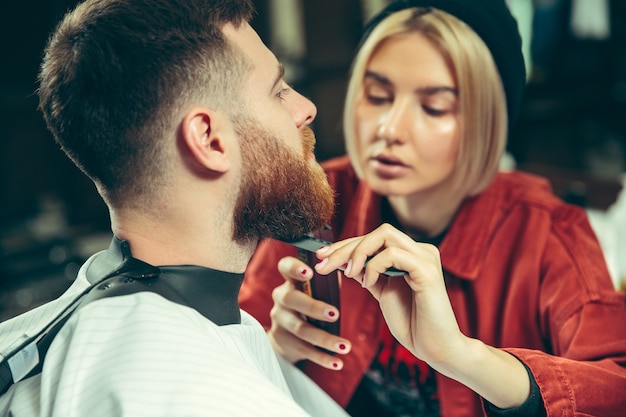 Client pendant le rasage de la barbe dans le salon de coiffure. Barbier féminin au salon. Égalité des sexes