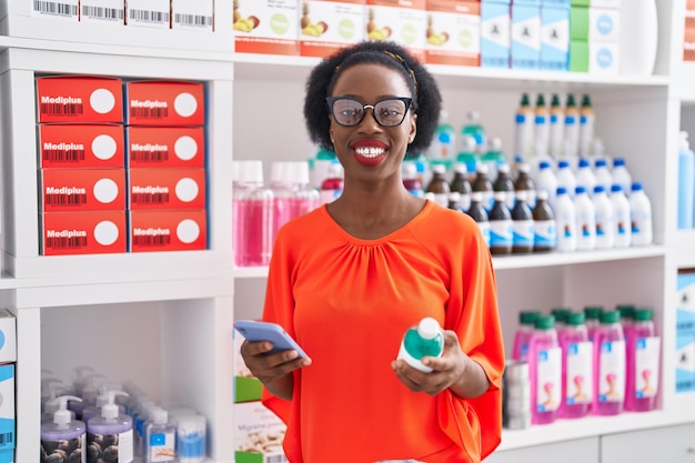 Cliente afro-américaine utilisant un smartphone tenant une bouteille de médicament à la pharmacie