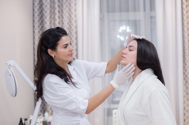 Une cliente lors d'un rendez-vous esthéticienne, consultation, mise en forme du visage, préparation aux procédures à venir, examen visuel des zones à problèmes