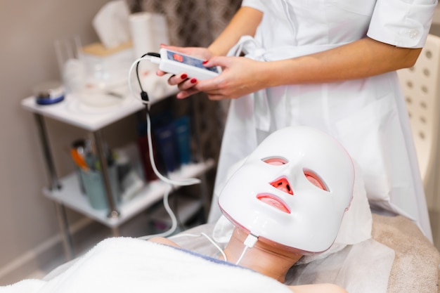 La cliente se trouve dans le salon sur la table de cosmétologie avec un masque blanc sur son visage