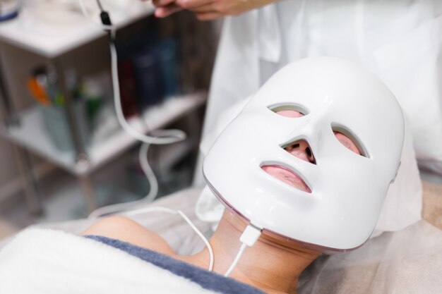 La cliente se trouve dans le salon sur la table de cosmétologie avec un masque blanc sur son visage