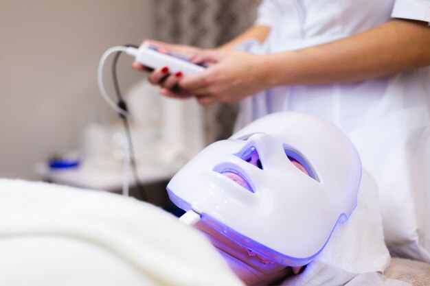 La cliente se trouve dans le salon sur la table de cosmétologie avec un masque blanc sur son visage