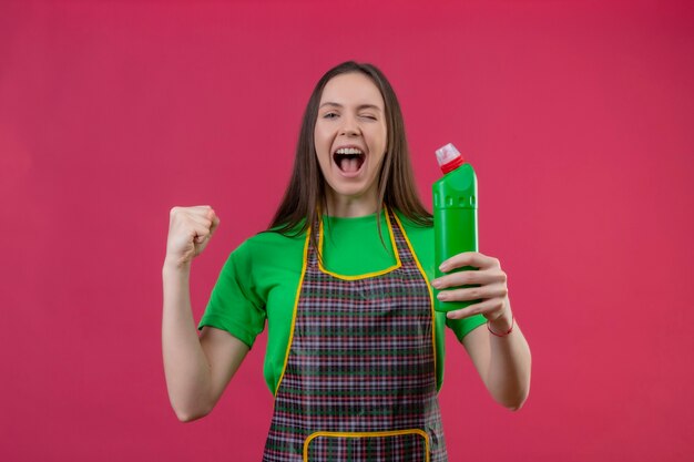 Clignoté joyeux nettoyage jeune femme en uniforme tenant un agent de nettoyage montrant oui geste sur mur rose isolé