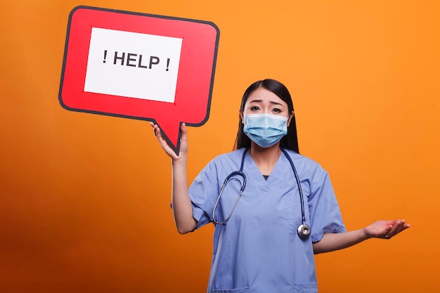 Photo gratuite une clinique de soins de santé a effrayé une infirmière portant un stéthoscope et des vêtements médicaux demandant de l'aide. le soignant de l'hôpital tient une pancarte à bulles en carton tout en portant un stéthoscope et un uniforme médical.