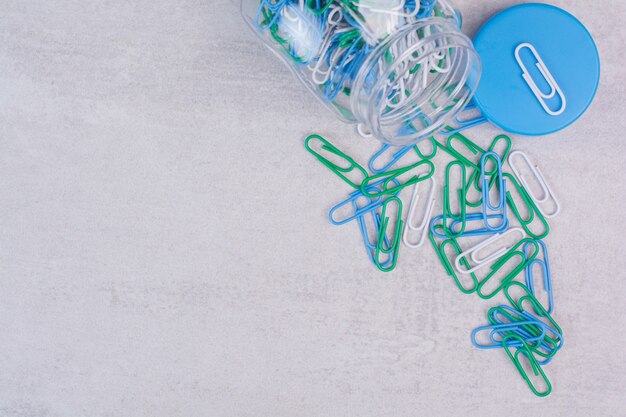 Clips colorés dans un bocal en verre sur blanc.