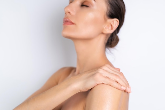 Close beauty portrait of topless woman with perfect skin holding bouteille de shampooing lotion appliquer sur les épaules et le corps sur fond blanc